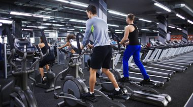 Two people exercising on an exercise bikes in front, and two people exercising on an elliptical machines at the back in the gym.