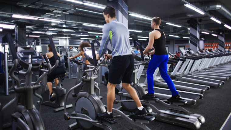Two people exercising on exercise bikes, and two people exercising on elliptical machines in the gym.