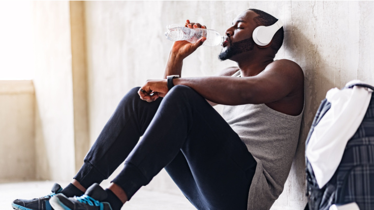 A fit person drinking water while sitting, listening to music.