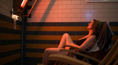 A person sitting in a room in front of an infrared sauna lamp.