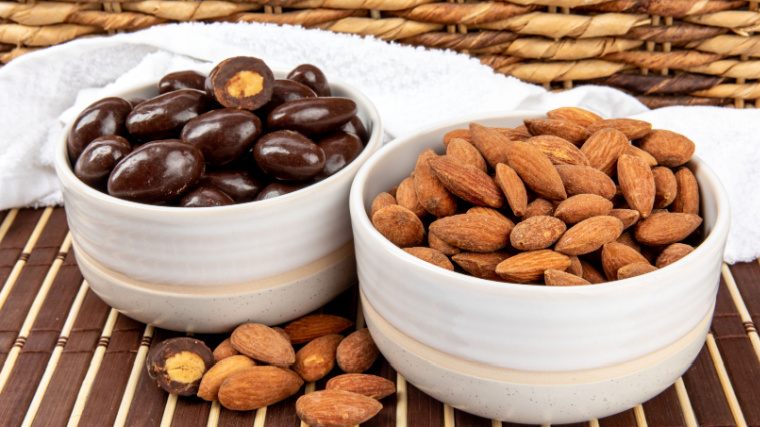 A bowl of plain roasted almonds and a chocolate covered almonds