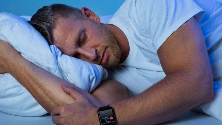 A person sleeping with a smart watch showing his heart rate.