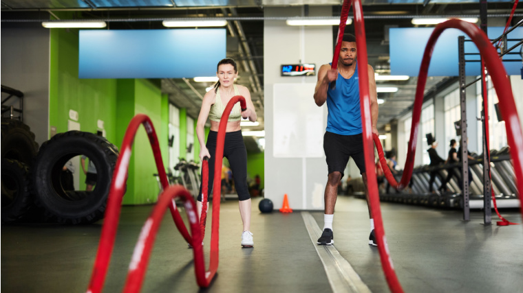 Two people exercising with battle ropes inside the gym.