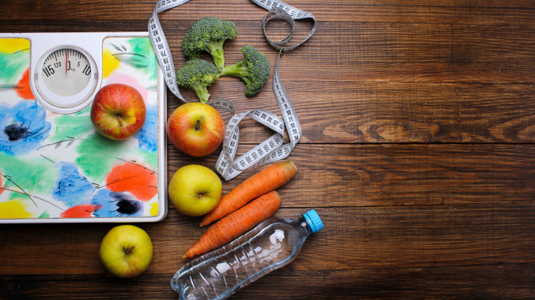 A scale, broccolis, apples, measuring tape, carrots and a water bottle.