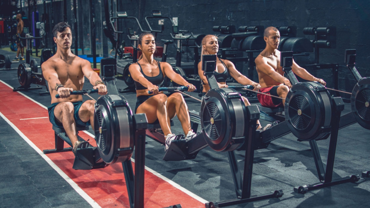 A group of muscular people working out on a rowing machine in the gym.