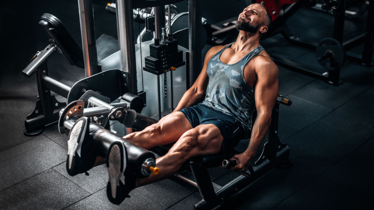 A muscular person working his legs out in the gym with a weight machine.