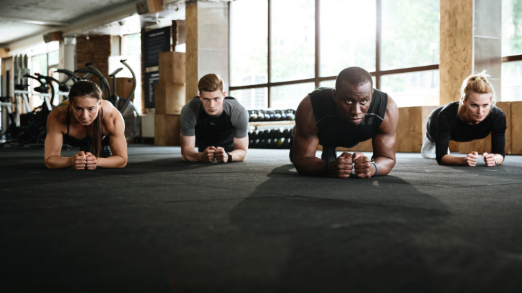 A group of fit individuals working out in the gym doing a plank exercise.