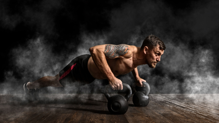 A muscular person doing push ups on kettlebells in the gym.