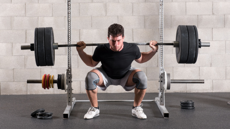 An athlete doing a back squat with a loaded barbell.