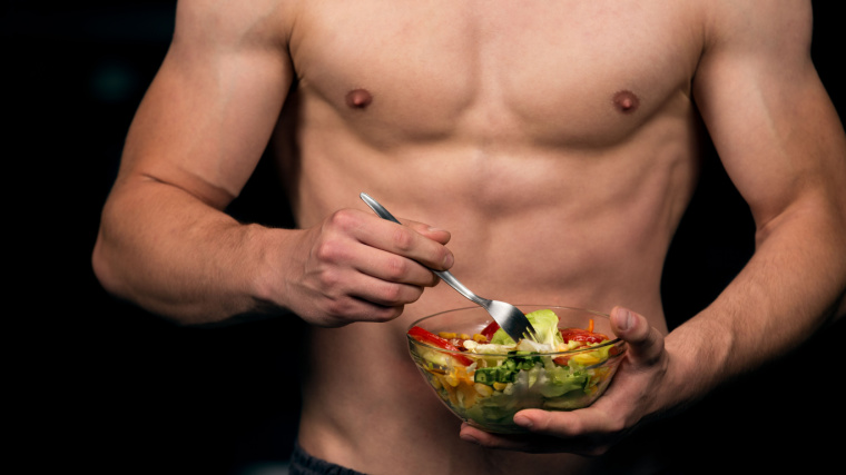 Shaped and healthy bodybuilder holding a fresh salad bowl.