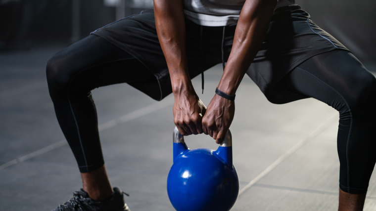 Strong adult person swing kettlebell to do CrossFit exercise.