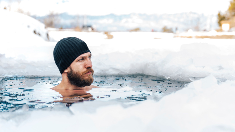 A person with beard taking a cold plunge in a frozen lake during winter.