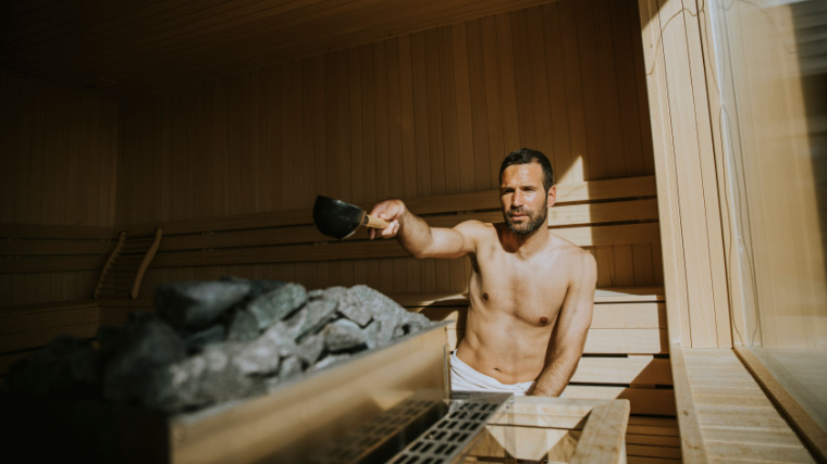 A person pouring water onto hot stone in the sauna.