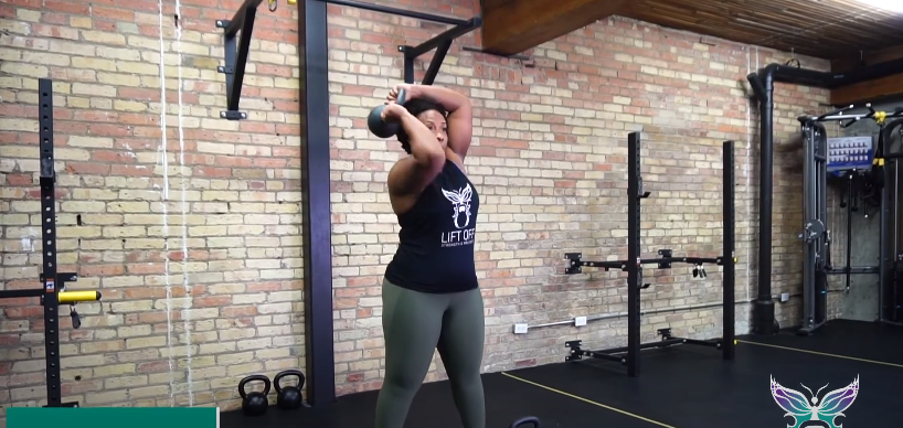 A fit person doing the kettlebell halo exercise in the gym.