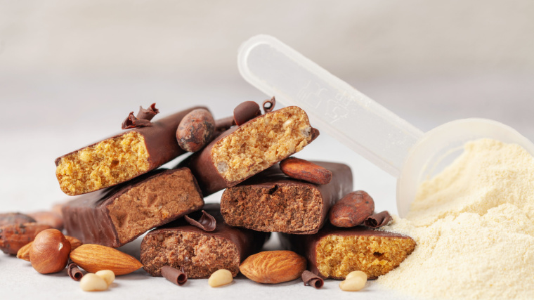 Whey protein powder in measuring scoop, nuts and different energy protein bar on grey background.