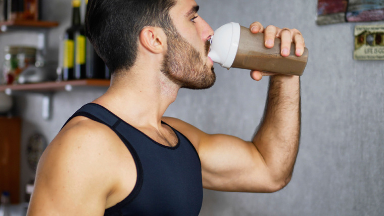 A muscular person drinking a protein shake from a shaker bottle.