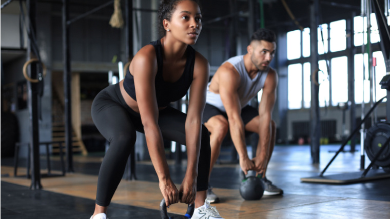 Two fit individuals starting to deadlift with kettlebells.