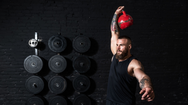 A muscular man doing the kettlebell snatch workout training in the gym.
