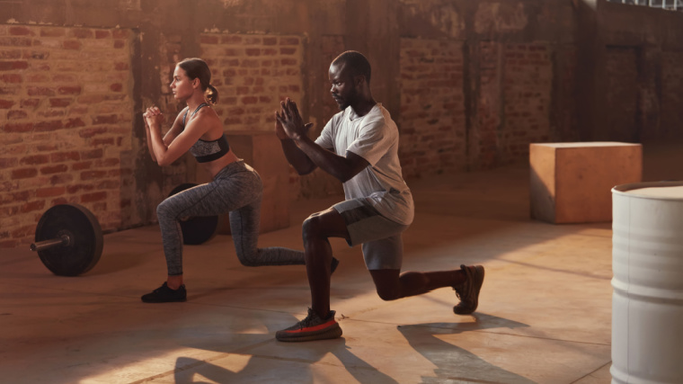 Two fit people doing the  lunge exercise in the gym.