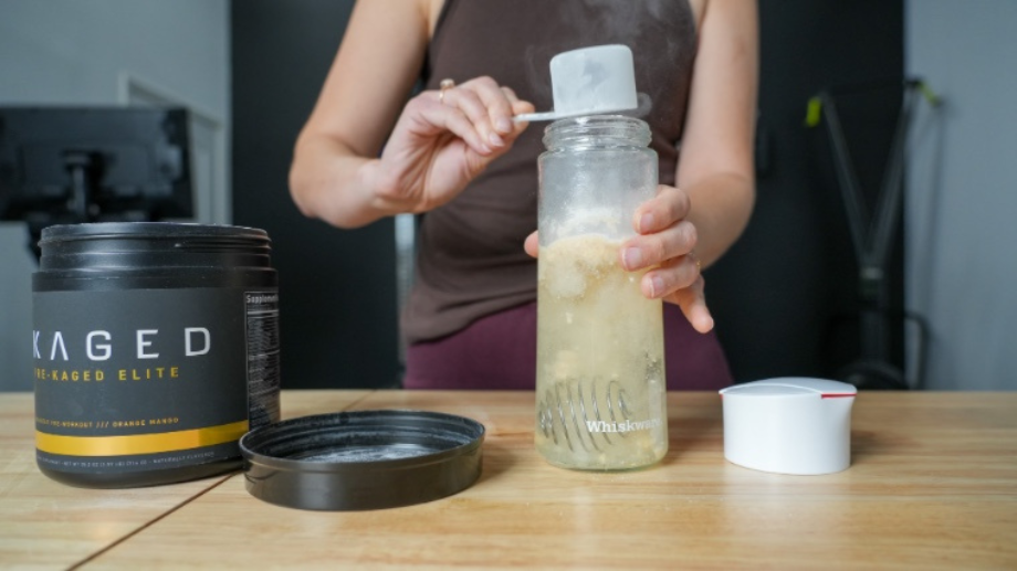An athlete scooping and mixing Kaged pre-workout.