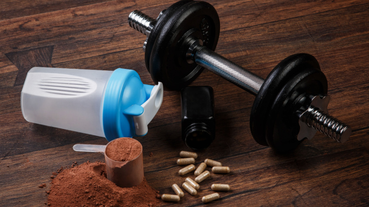 Pre-workout powder, tablets, container and a dumbbell.