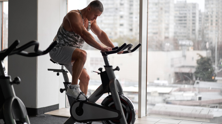 A muscular person using an upright bike.