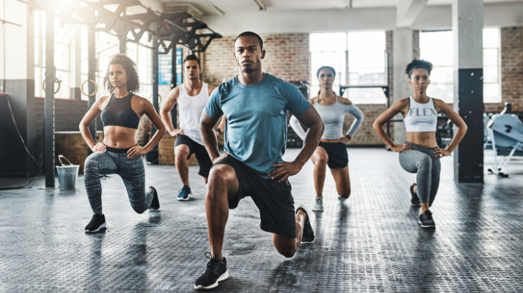 A group of fit people doing lunge exercises in the gym.