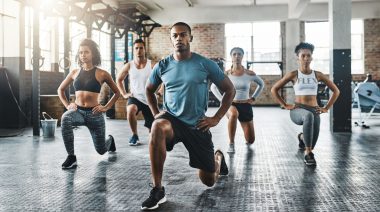A group of fit people doing lunge exercises in the gym.