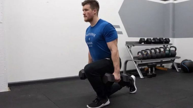 A coach doing the walking lunge with a pair of barbells.