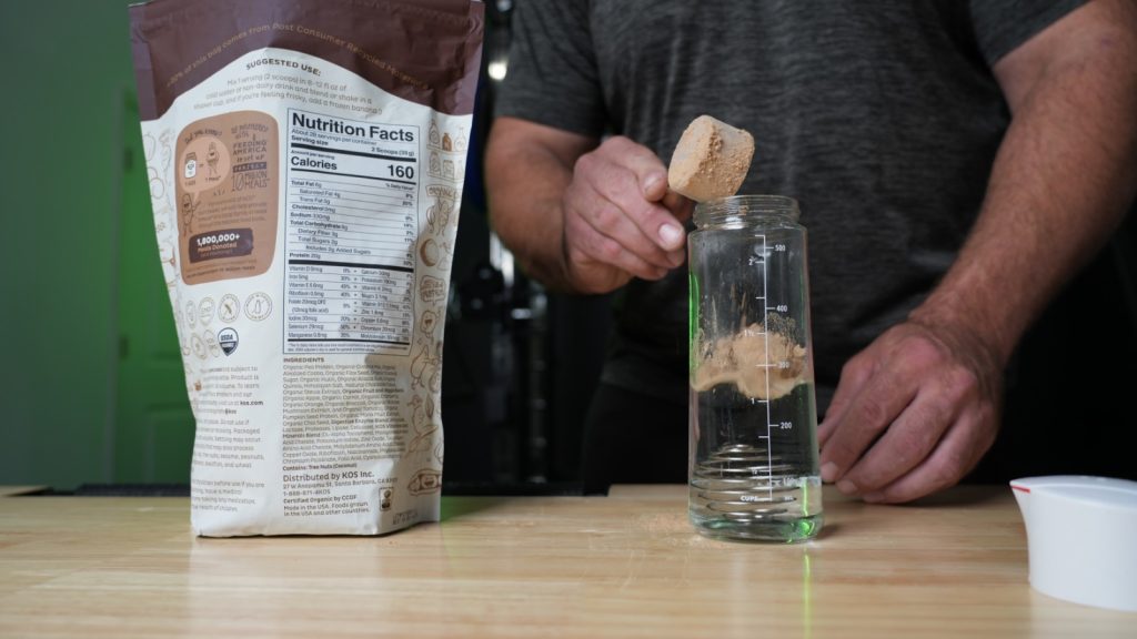 Our tester takes a scoop of KOS Vegan Protein Powder into a glass of water.