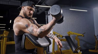 A bodybuilder doing a preacher curl with a dumbbell.