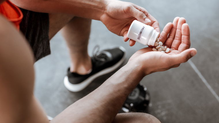 An athlete holding a bottle with probiotic lettering and pills in the gym.