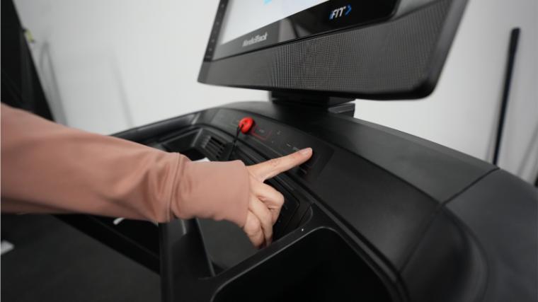 A person's hand is shown adjusting settings on the Commercial 2450 2023 model treadmill.