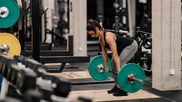 A fit individual deadlifting a barbell in the gym.