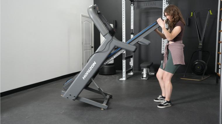 A woman unfolds a Horizon 7.4 AT Unfolding Treadmill.
