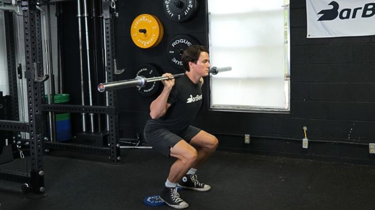 A person performing heel elevated back squat exercise.