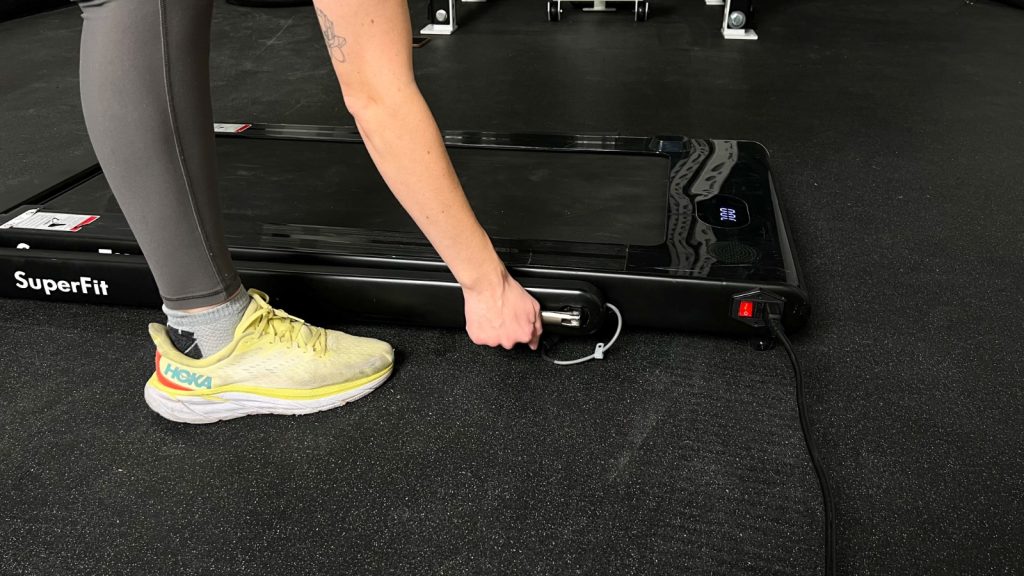 A person reaches down, unlatching the handlebar on the Goplus 2 in 1 Folding Treadmill.