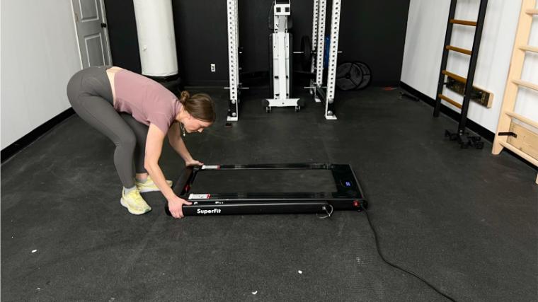 A woman in a gym reaches down grabbing the handle bar on a SuperFit Treadmill