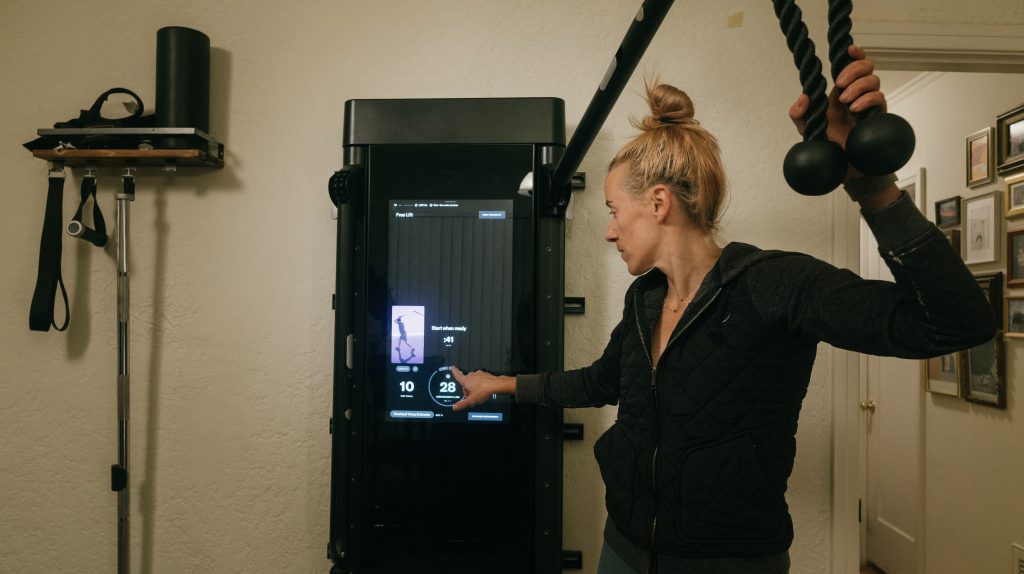 A woman changes the weight on a Tonal smart gym.