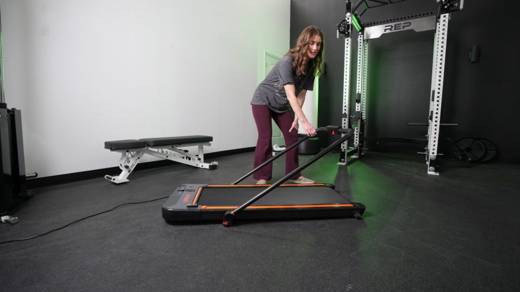 A person lowers the handlebar on the UREVO 2-in-1 Under-Desk Treadmill.