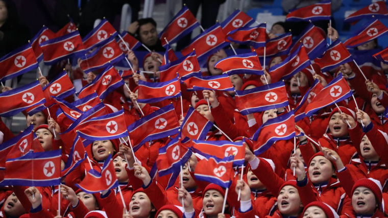 North Korean fans wave flags in stadium at athletic event. 