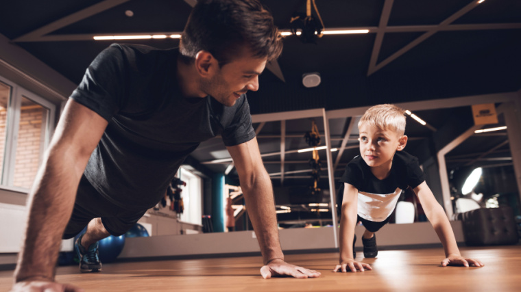 Adult man does push-ups with blonde child in exercise studio
