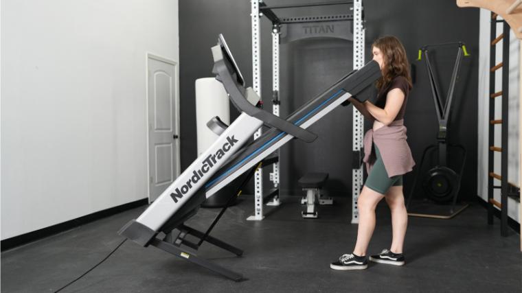 A woman is shown unfolding the NordicTrack EXP 7i Treadmill.