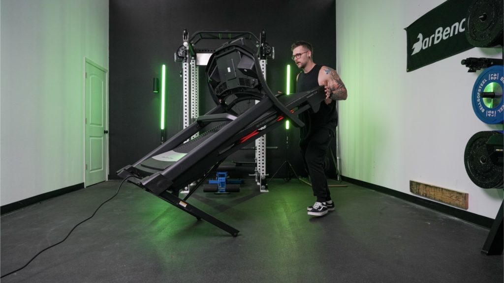 A person is shown in the process of unfolding a ProForm Trainer treadmill.