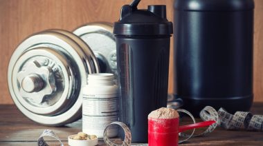 Measuring tape, dumbbell, shaker, tablets and a scoop full of powdered supplements.