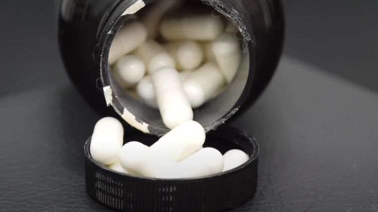 An open bottle of creatine pills poured over the bottle cap.