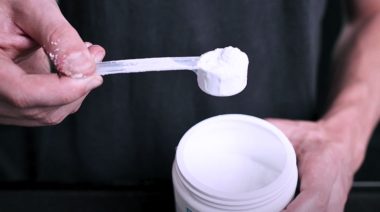 A person taking out a scoop of creatine powder from a container. Image for the article that asks does creatine help you lose weight?