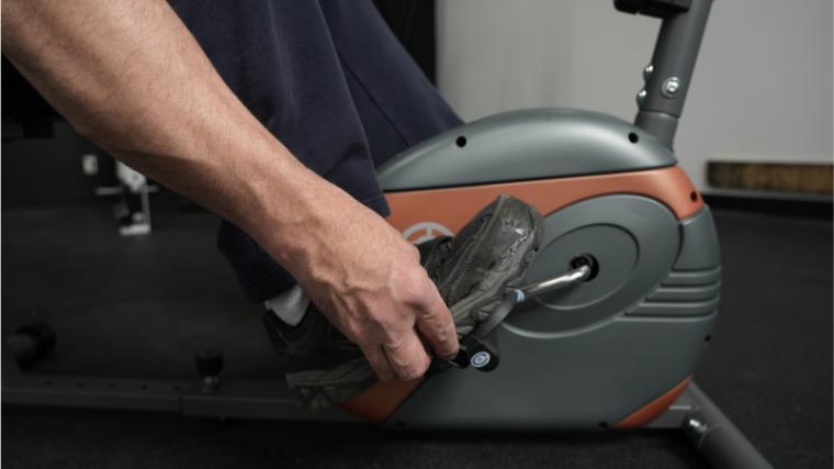 Our BarBend tester adjusting the foot strap on the pedals of the Marcy ME-709.