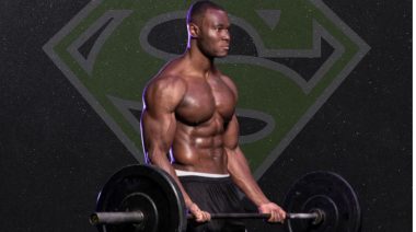 A person in front of a green "Superman" logo curling a loaded barbell.