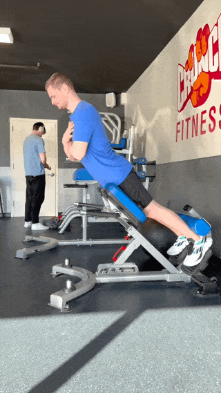 Person in blue shirt and black shorts performing back extensions on a back extension pad.